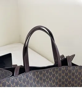 Detailed close-up of dark brown tote bag with M-pattern monogram and sturdy leather handles