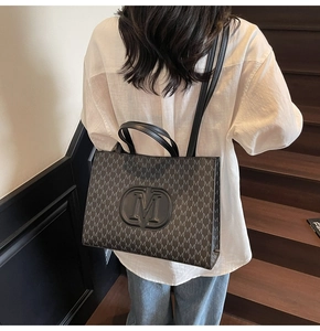 Detail of black printed tote bag with M letter pattern shown on a female model