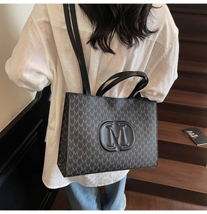 Detail view of large black tote bag with M-pattern monogram and embossed round logo detail