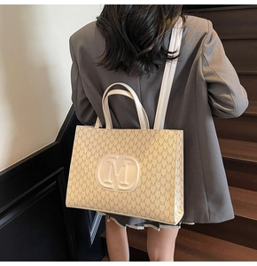 Model showing large monogram tote bag in beige with shoulder strap on stairs