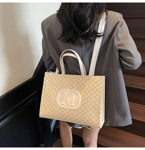 Detail of beige monogram tote bag with relief logo and leather shoulder strap handles