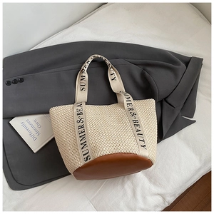 Détail d'un sac cabas en paille tissée avec base en cuir marron et sangle imprimée