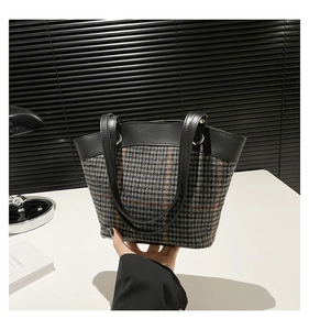 Classic houndstooth tote bag with black leather trim held by a model in a retro setting