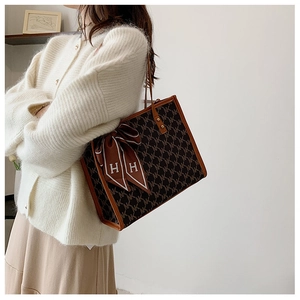 Detail of monogram tote bag with brown leather trim and decorative silk scarf on handle