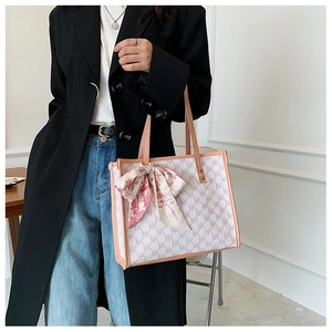 Close-up of cream tote bag with NK pattern, leather trim and floral silk scarf detail