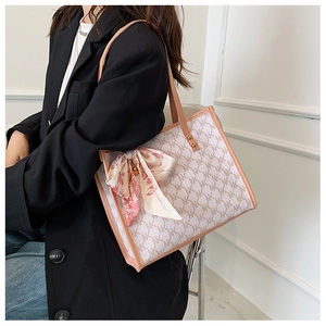 Detail of a beige tote bag with NK logo print and decorative floral scarf on the handle