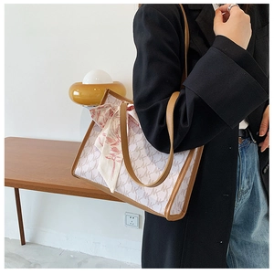 Detail of monogram tote bag with pink floral scarf on brown leather handle