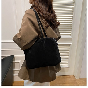 Side view of a model wearing a matte black leather shoulder bag with long straps