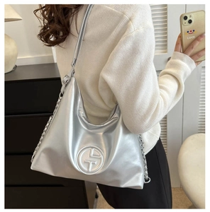 Detail der silbernen Metallic-Tasche mit Kettenriemen und Logo-Prägung am Model