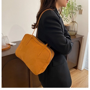 Side view of mustard orange faux suede square shoulder bag worn by model in home studio