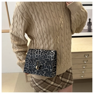 Fashionable leopard print crossbody bag with gold chain strap on a wooden cabinet