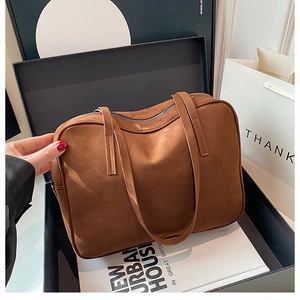 Detail of a brown suede rectangular handbag placed inside a premium black gift box