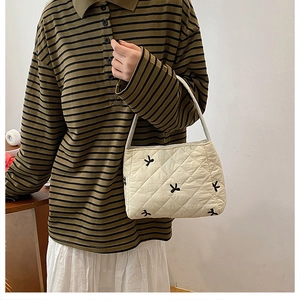Detalle del bolso acolchado crema con elegantes bordados de lazos negros y asas finas