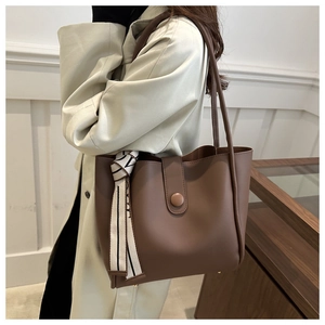 Detail of a brown leather tote bag with a decorative silk scarf and metallic closure
