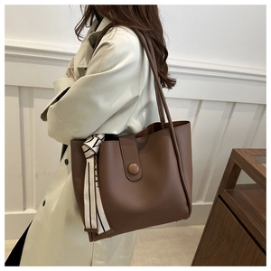 Detail of dark brown tote bag with decorative patterned scarf handle on white background