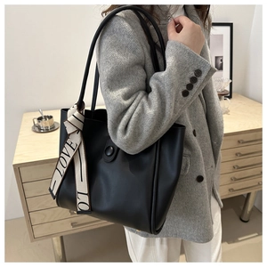 Detail of black leather tote bag with LOVE silk scarf on handle worn with winter coat