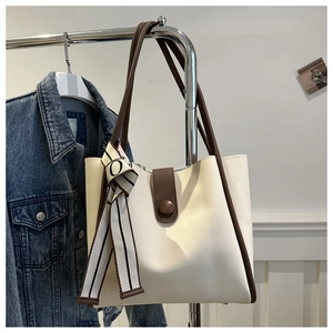 Detail of white leather tote bag featuring brown trim and a striped silk scarf accessory
