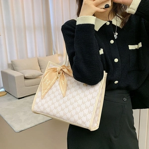 Chic beige tote bag with monogram print and decorative silk scarf shown on shoulder