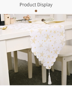 Détail d'un chemin de table de Noël blanc avec étoiles dorées, bords festonnés et gland