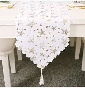 Détail du chemin de table blanc avec étoiles dorées, bords festonnés et glands