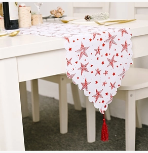 Détail d'un chemin de table de Noël blanc avec étoiles rouges, bords ondulés et pompon