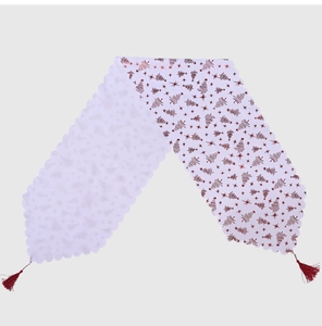 Détail d'un chemin de table de Noël blanc avec motifs sapins rouges et glands rouges