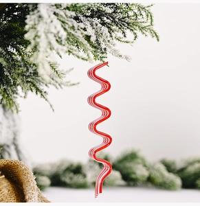 Detail of red and white spiral candy Christmas ornament hanging on a snowy pine branch