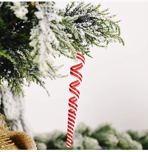 Detail of red and white spiral icicle candy cane hanging on snow-covered Christmas tree