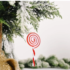 Detail of red and white spiral candy ornament hanging on a snowy Christmas pine branch