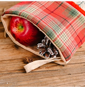 Close-up of red and green plaid linen Christmas stocking with a red apple and pine cones
