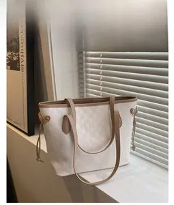 Detail of white checkered tote bag with brown leather handles and golden metal hardware