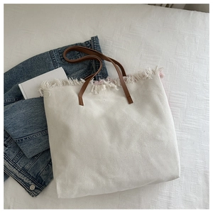 Detail of cream canvas tote bag with fringe edge and brown leather handles on denim