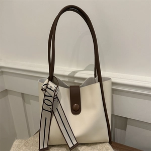 Minimalist beige leather tote bag with brown trim and love ribbon on a wooden surface