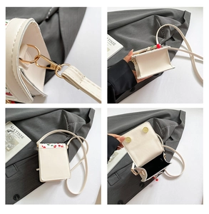 Detailed views of mini white leather crossbody bag with cherry prints and gold hardware