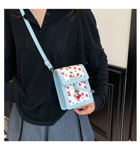 Detail of light blue crossbody bag featuring cherry print and golden fashion logo