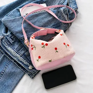 Detail of pink corduroy shell bag featuring red cherry embroidery and leather base