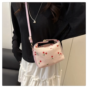 Close-up of pink corduroy crossbody bag with red cherry patterns and gold hardware detail
