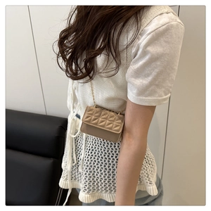 Detalle de un mini bolso beige acolchado con una delgada correa de cadena dorada elegante