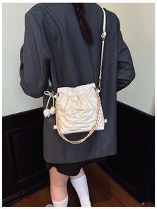 Close-up of white quilted bucket bag featuring a gold chain and tulip charm detail