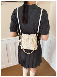 Detail of cream quilted bucket bag with tulip pendant and gold chain on model