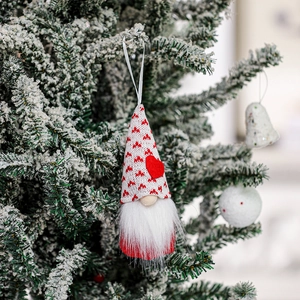 Close-up of a handmade Valentine gnome ornament hanging on a snowy green pine branch