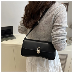Close-up of black matte leather shoulder bag featuring a gold oval clasp on a desk
