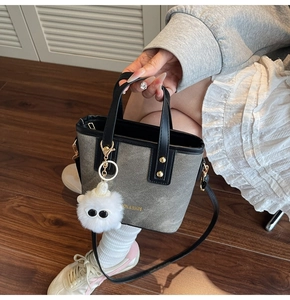 Detail of grey canvas bucket bag with black leather trim and fuzzy eye monster charm