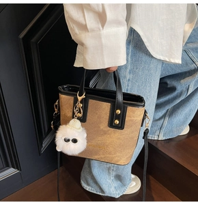 Close-up of a brown textured bucket bag with gold lettering and a plush charm
