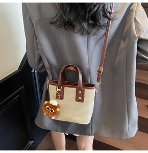 Close-up of beige canvas bucket bag with brown leather trim and cute lion charm detail