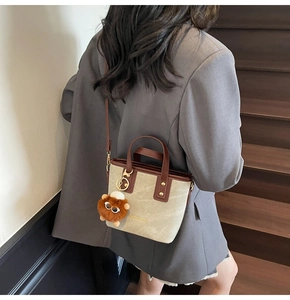 Detail of canvas bucket bag with leather trim and brown plush lion charm accessory