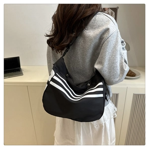 Détail d'un sac bandoulière noir sportif avec trois bandes blanches et une sangle large