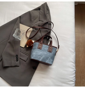 Detail of denim bucket bag with brown leather trim and plush pom-pom charm on a blazer