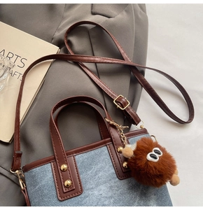 Detail of denim bucket bag with leather handles and a plush monster charm on fabric background