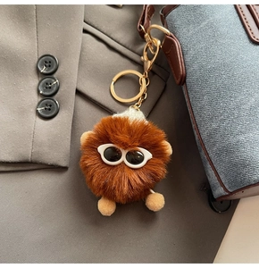 Close-up of brown plush charm with glasses on denim bag, gold metal keychain detail